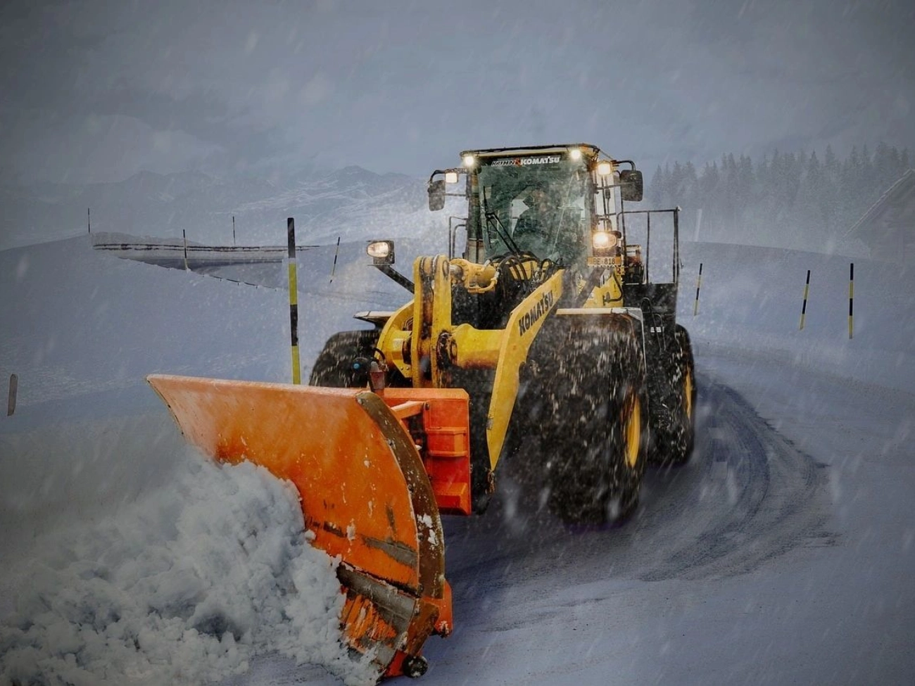 A yellow and black tractor with snow plow in the background.